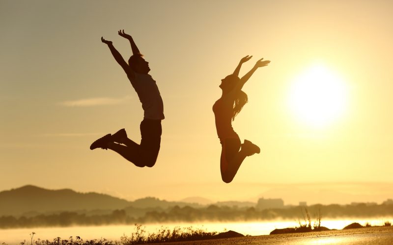 Fitness couple jumping happy at sunset with the sun in the background